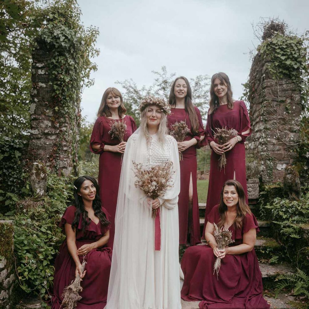 Bride in long sleeve lace wedding dress with church length veil standing with bridesmaids in burgundy mid length sleeve bridesmaid dresses at Pagan wedding