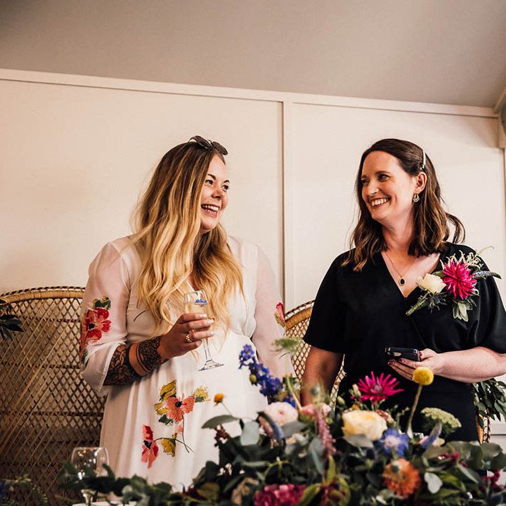 Bride in colourful embroidered floral wedding dress with bride in black jumpsuit standing at their sweetheart table 