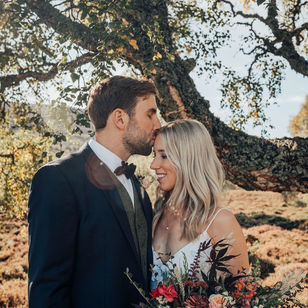 Groom kisses bride on the forehead whilst she holds Autumnal coloured bouquet 