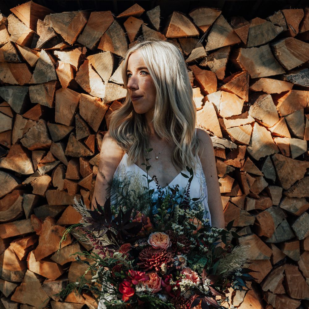 Blonde bride holding Autumnal bouquet in front of logs