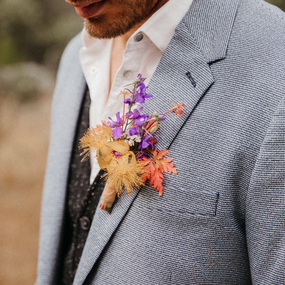 Groom wears colourful floral buttonhole tied with brown ribbon