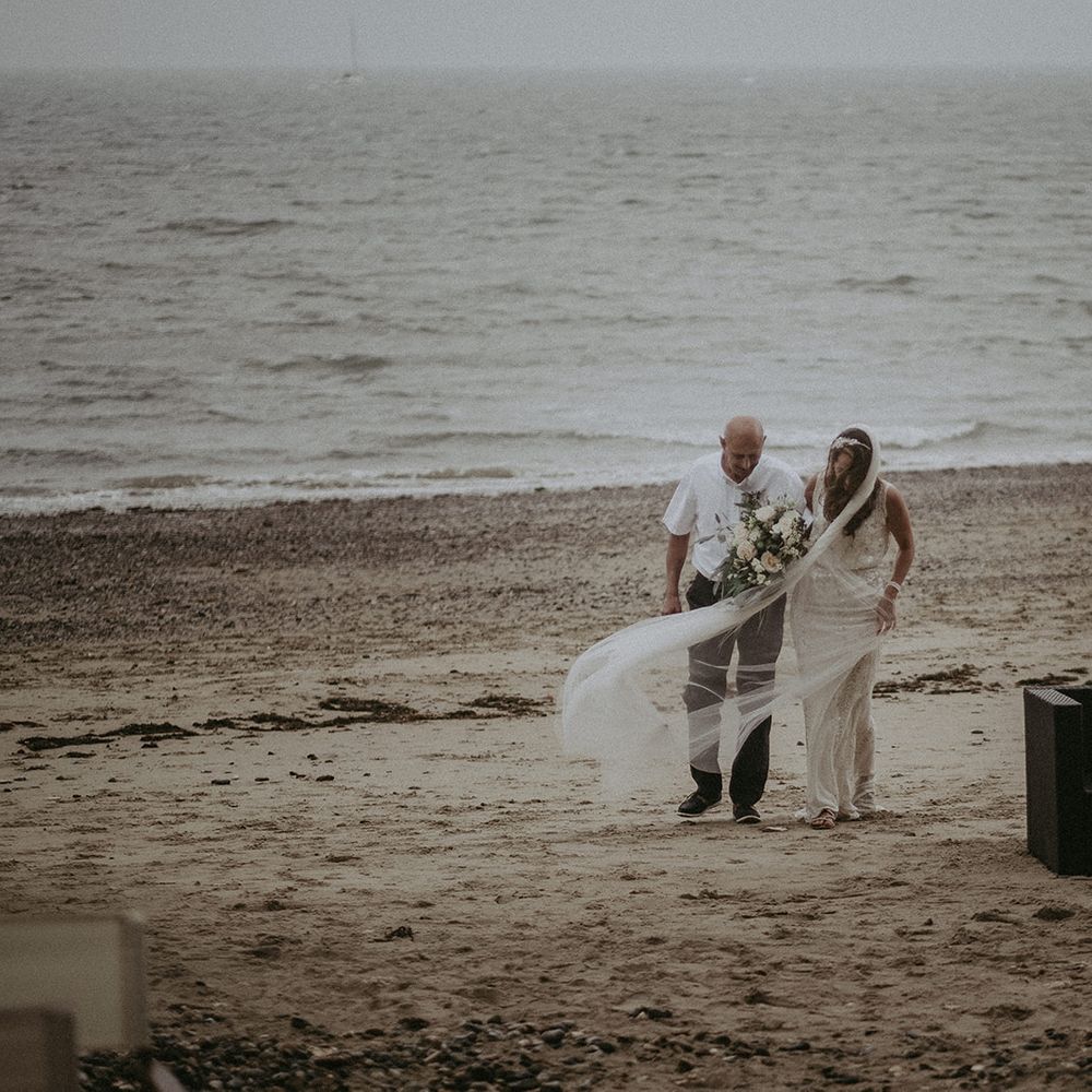 Bride & groom stand together on the beach on the day of their wedding