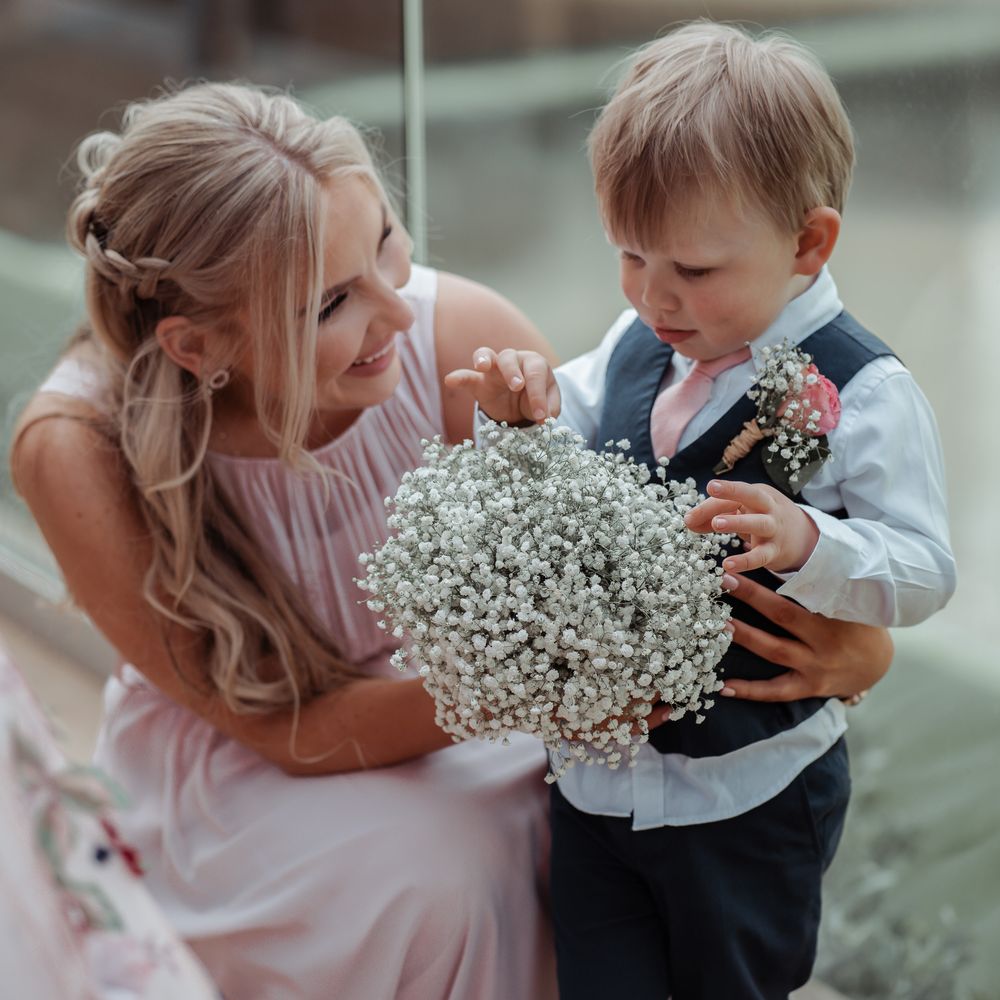 Bridesmaid stands with little boy in suit whilst looking at florals