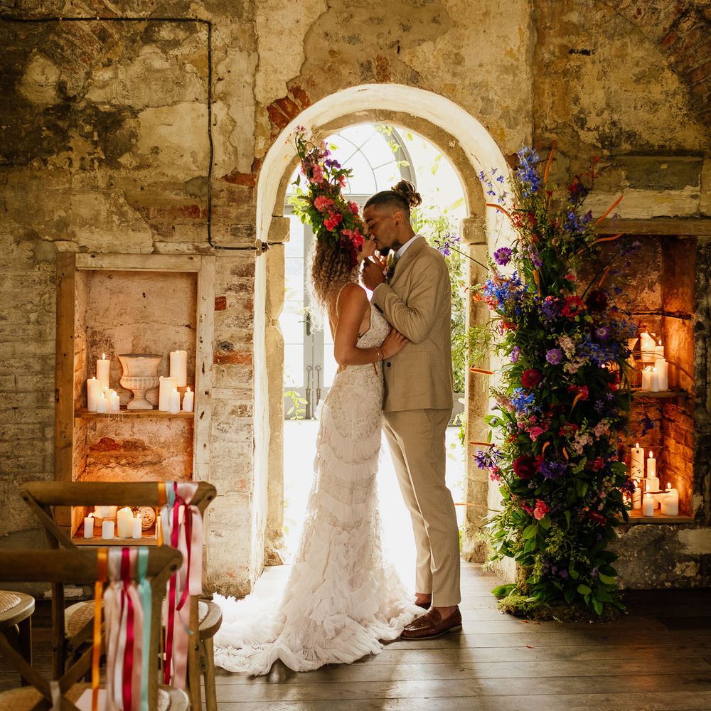 Bride and groom kissing in the intimate ceremony room with pillar candles, vertical floral arrangement and ribbon chair back decor 