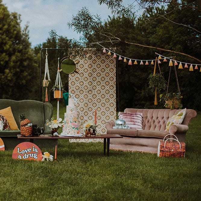 Sixties wedding inspiration outdoor seating area with bold prints, vibrant colours and retro decor including sofas, cushions, macrame, tassels and signs 