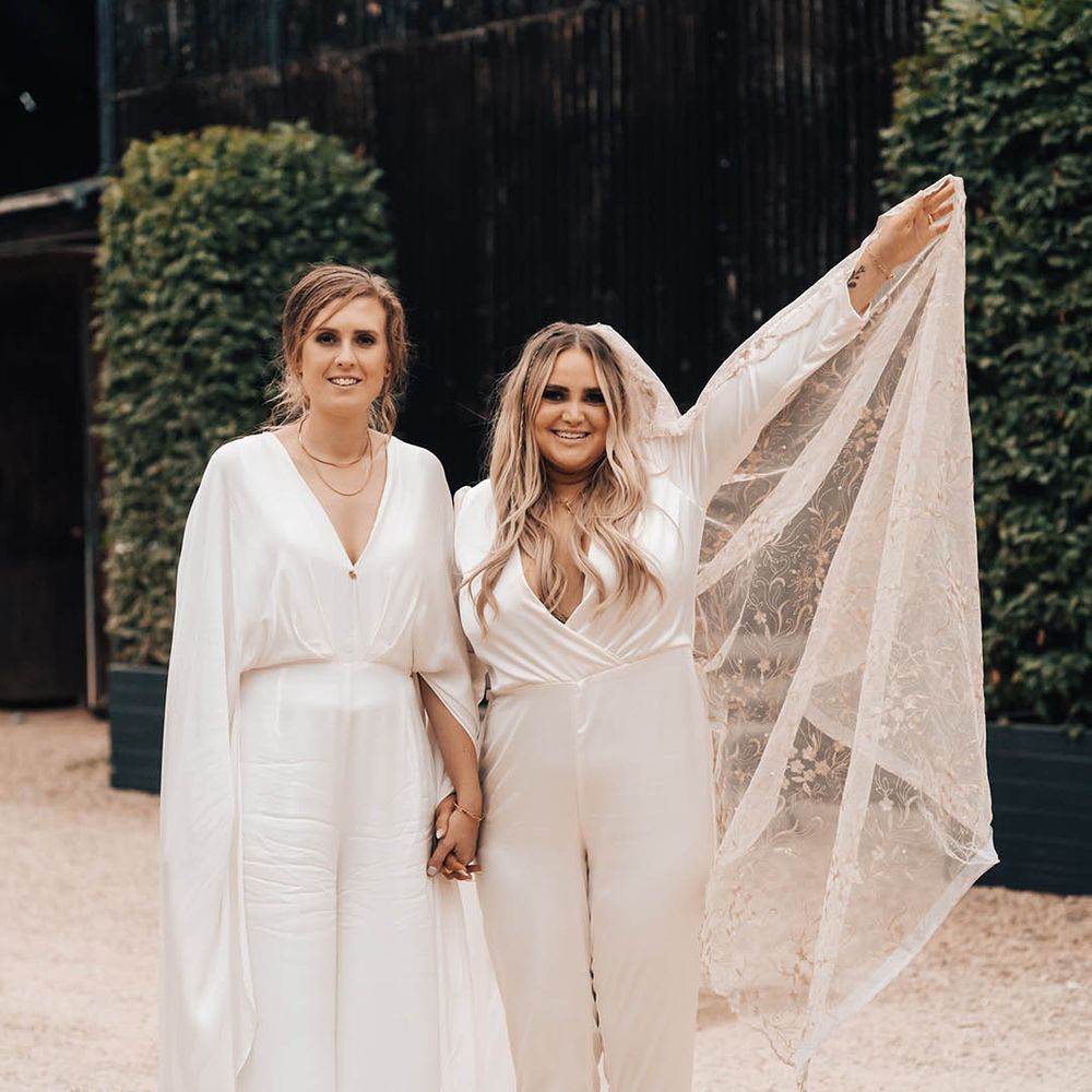 Bride lifts her veil in the air as she walks with her wife on their wedding day