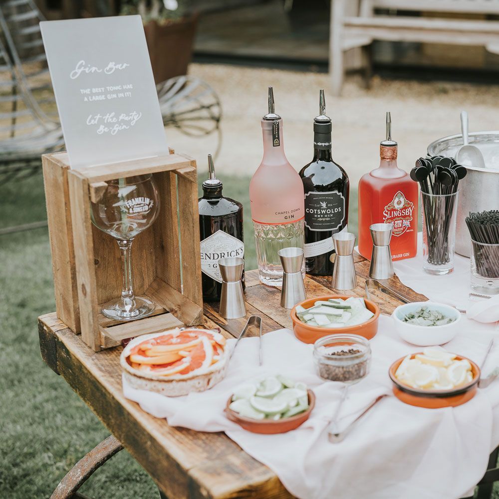 Make your own gin bar with gins, shot measures, garnishes and ice bucket on wooden table for Tythe Barn wedding with barn wedding flowers