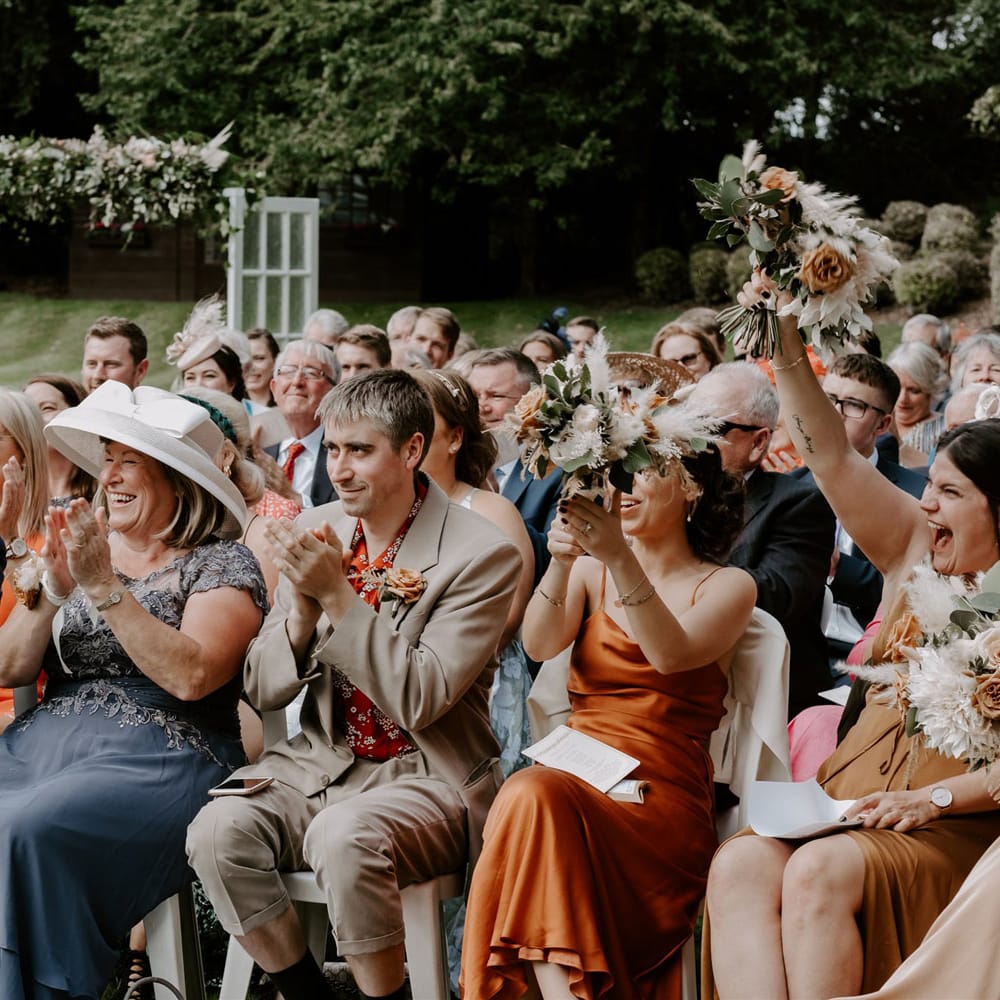 Various wedding guests smile and clap during DIY garden wedding ceremony in Bedfordshire