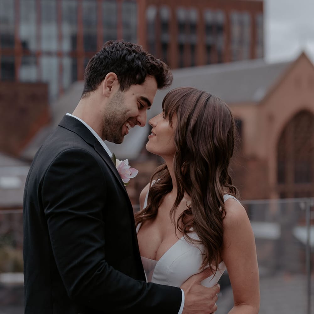 Groom in a black suit embracing his bride in a plunging neckline wedding dress with long wavy hair and fringe 