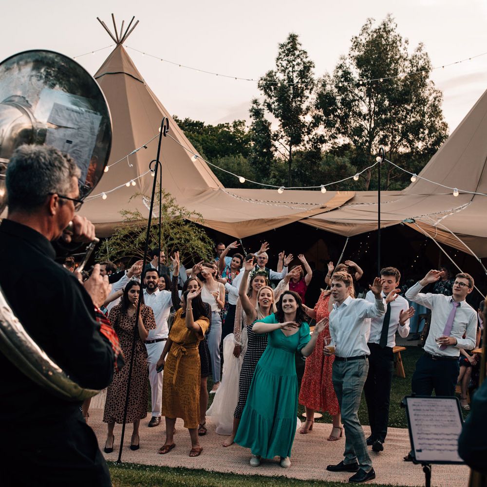 Wedding guests dance outside to brass band during tipi wedding reception 