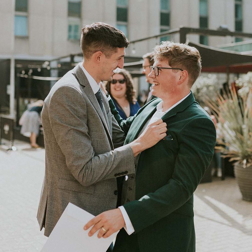 Groom celebrates with wedding guest who holds his jacket and smiles whilst laughing