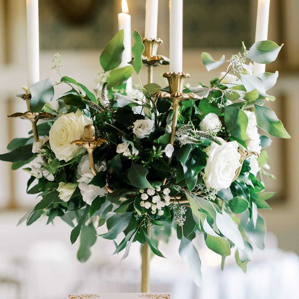 gold candelabra wedding centrepiece decorated with white flower and green foliage 