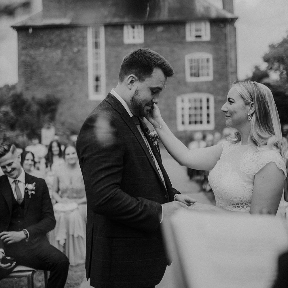 Outdoor wedding ceremony at Dewsall Court with bride in a Jesus Piero wedding dress embracing her grooms face 