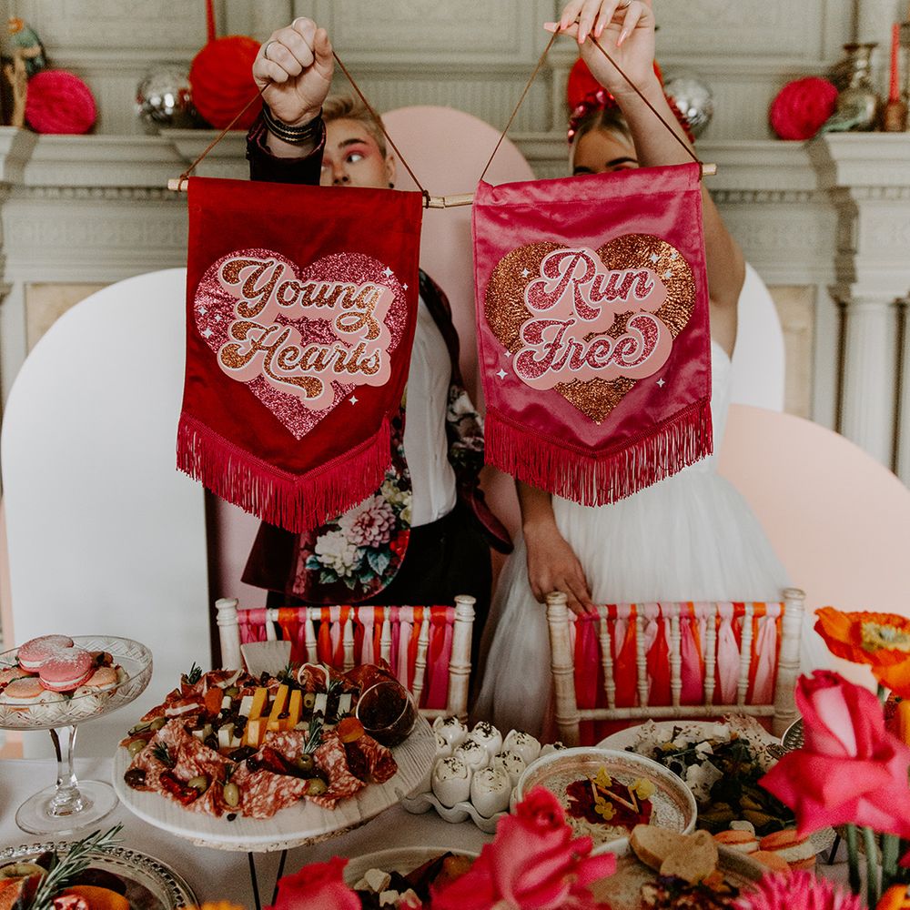 Two brides holding up velvet banners with tassels saying Young Hearts, Run Free