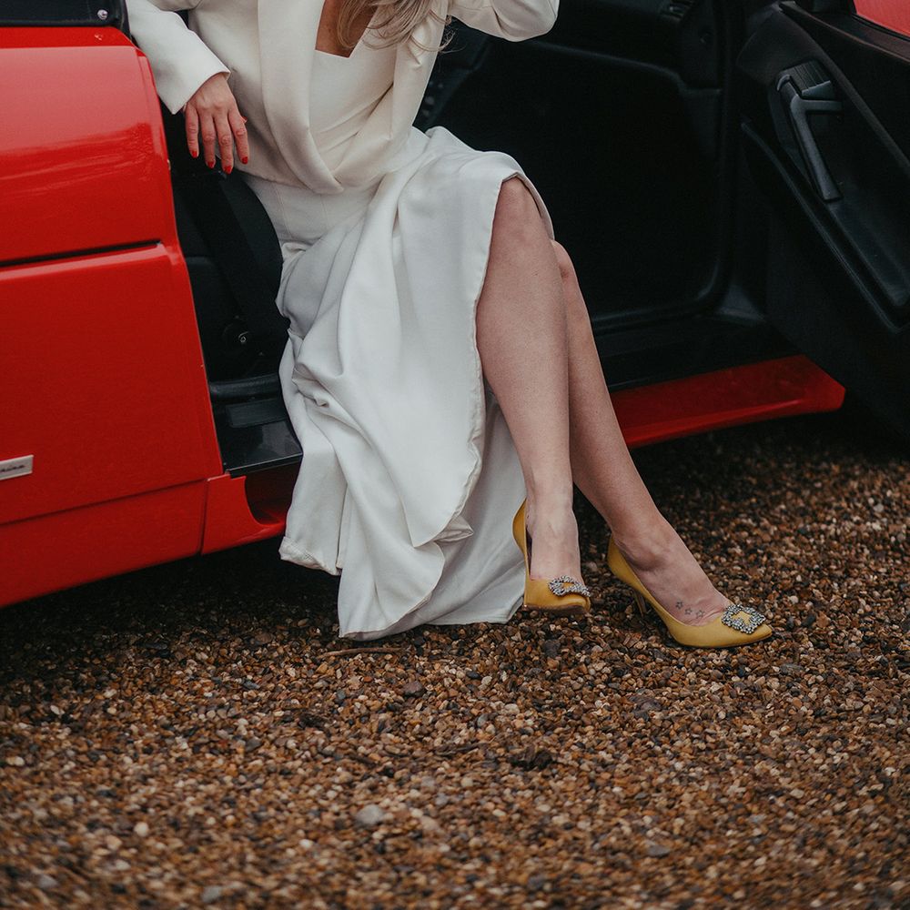 Bride sits in vintage Ferrari on her wedding day and wears yellow Malono Blahnik heels 