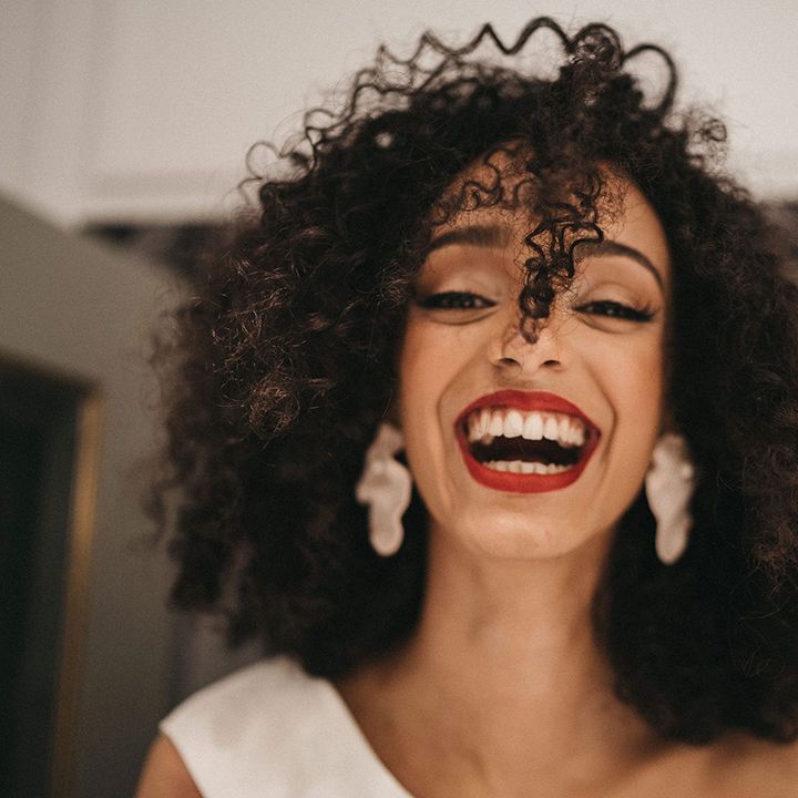 Black bride with naturally curly hair wearing dangly earrings and wearing red lipstick 