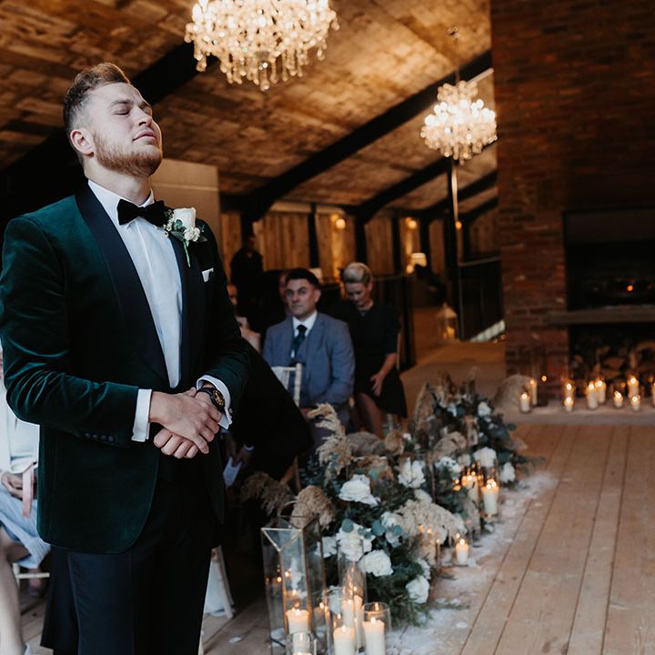 Groom in black tie including green velvet suit jacket nervously awaits the arrival of the bride at winter Christmas wedding