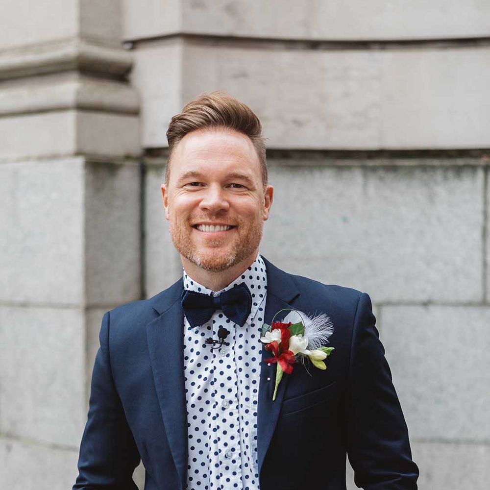 Groom wears deep blue suit with matching polka dot shirt and bow tie with floral buttonhole 