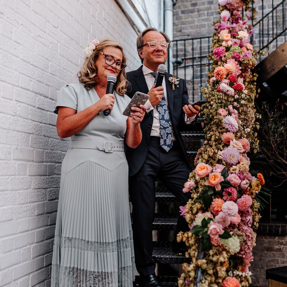 Mother and father of the bride giving a font wedding speech on the stair at the Loft Studios decorated in green and pink wedding flowers 