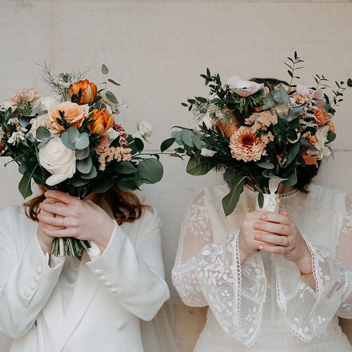 Brides hold up floral bouquets complete with pops of orange and white florals with green foliage