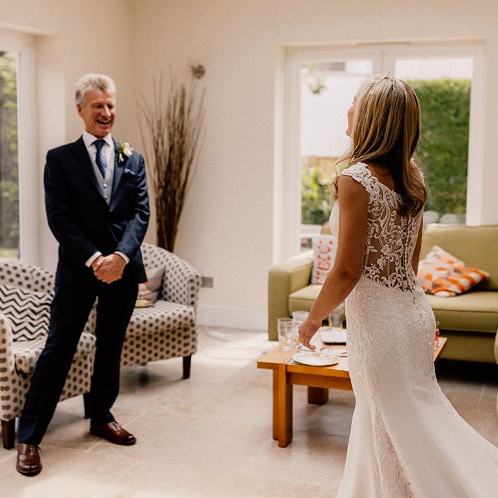 Bride enters the room wearing her sheer lace back wedding dress with button detail as father of the bride gets his first look 
