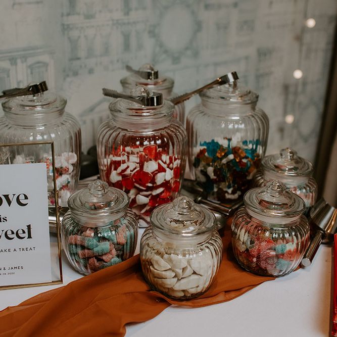 Sweets table complete with orange table runner and jars  full of sweets 