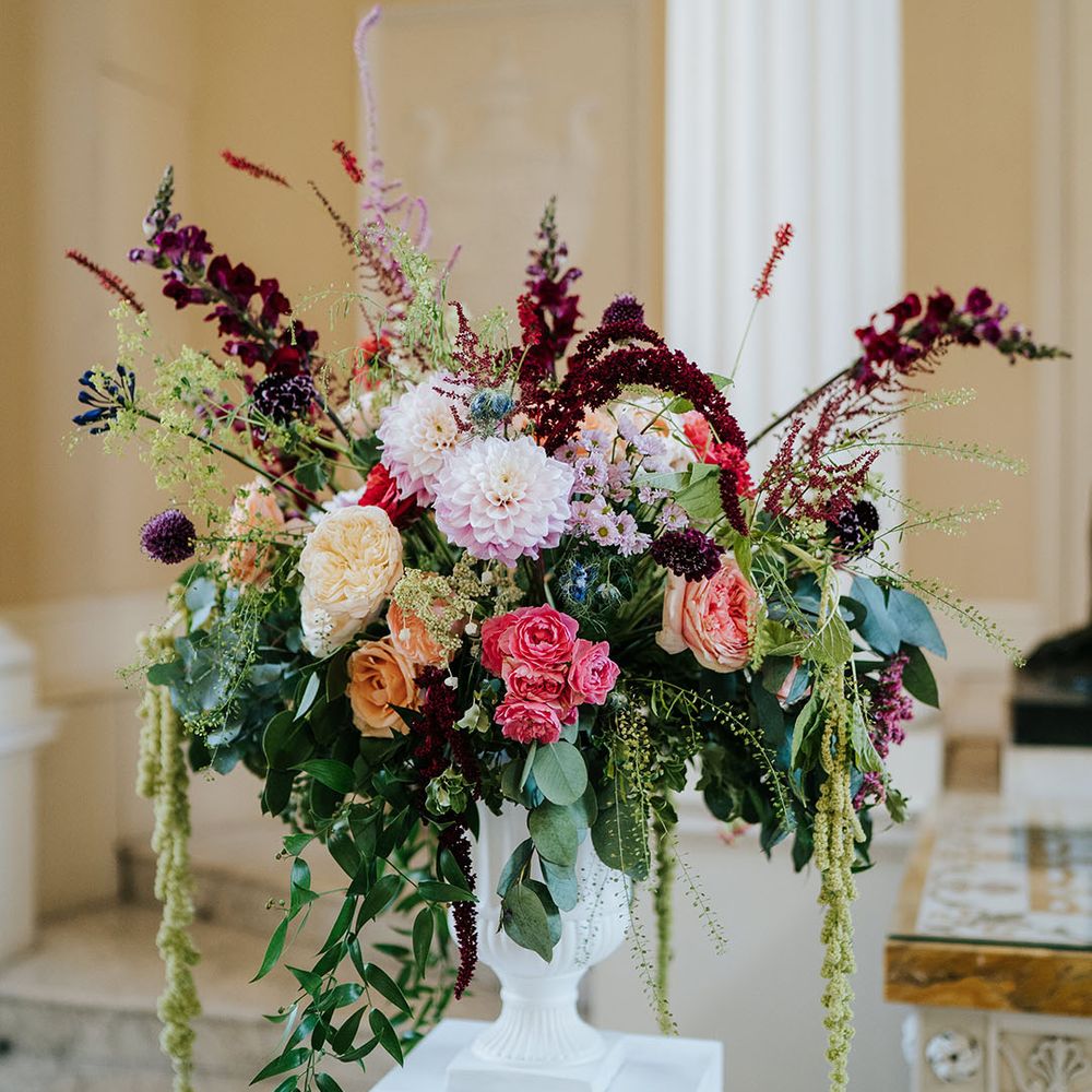 Brightly coloured floral bouquet complete with green foliage in white vase 