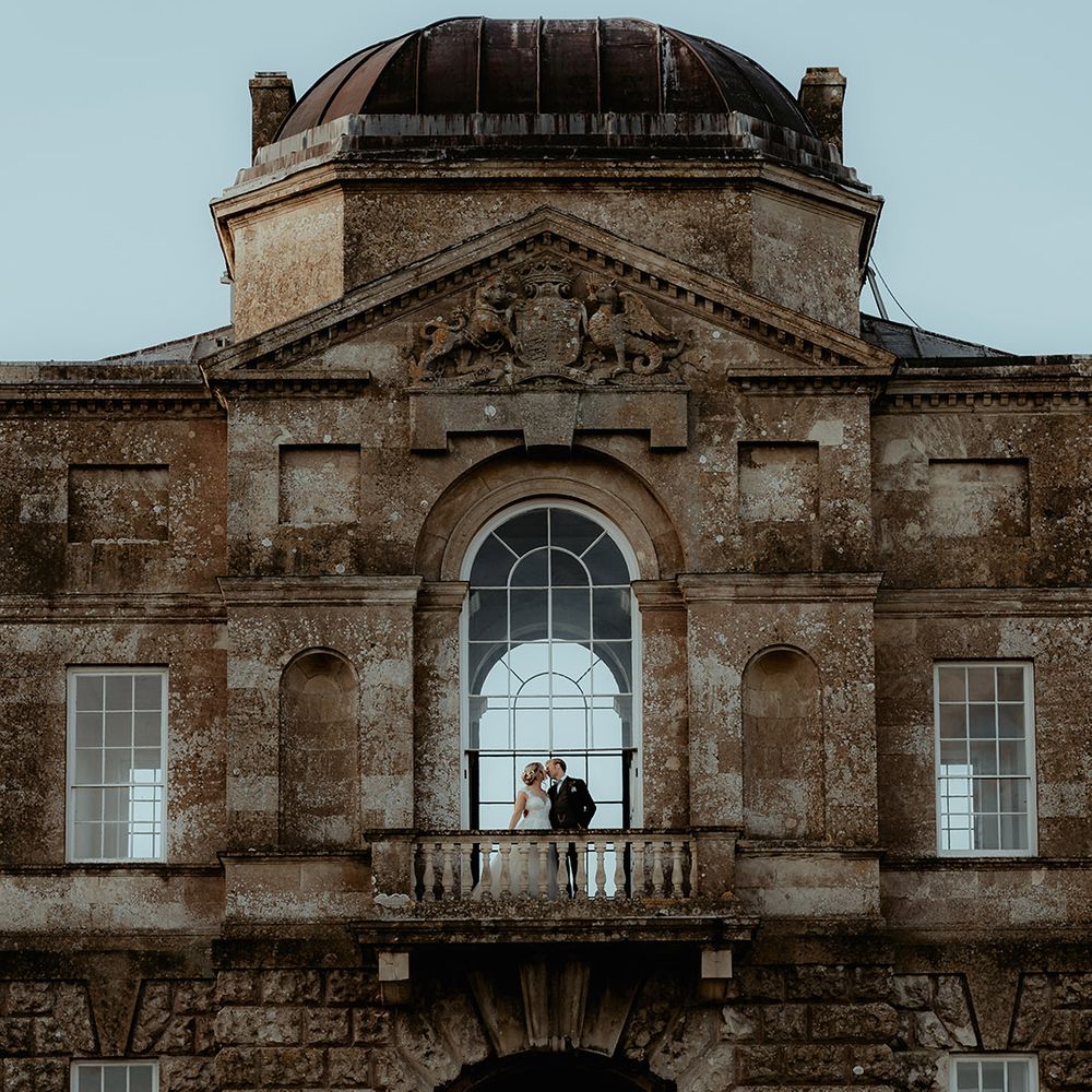 Badminton Estate wedding venue with the bride and groom standing on a balcony 