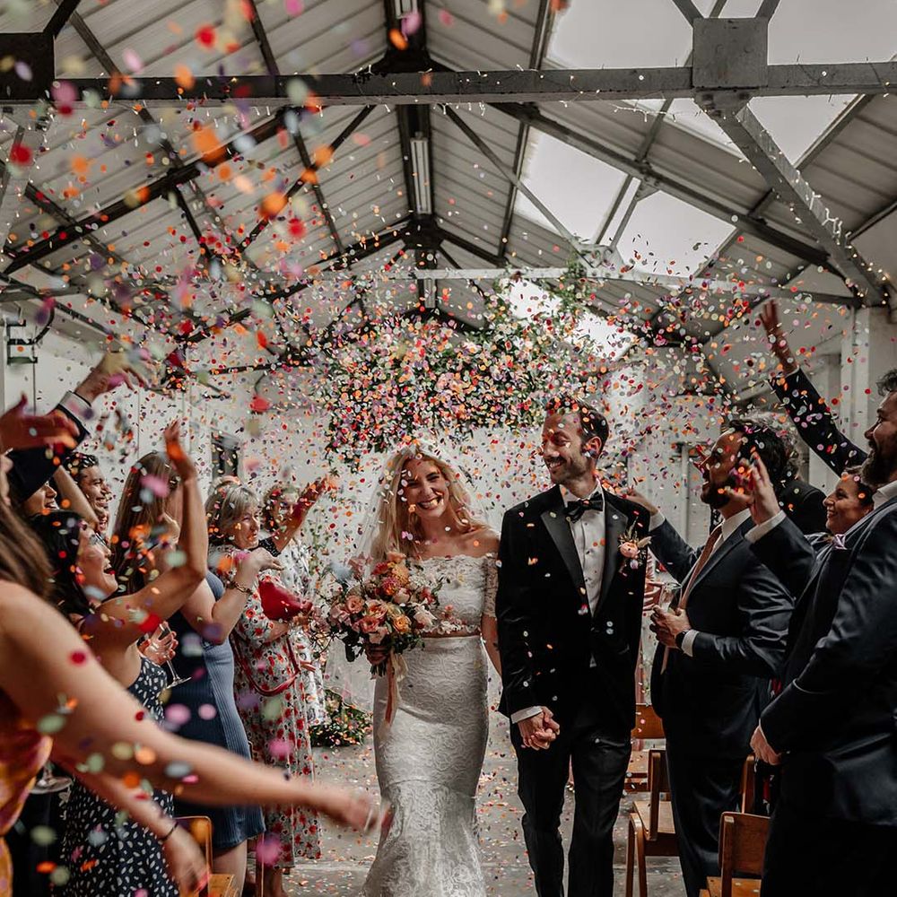 Bride in lace boho two piece and groom in black tux with bow tie and boutonniere doing confetti walk at Hackney Studios