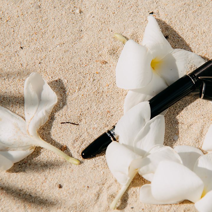 Tropical white flowers surrounding bride's father's black pen on the sand of Seychelles beach