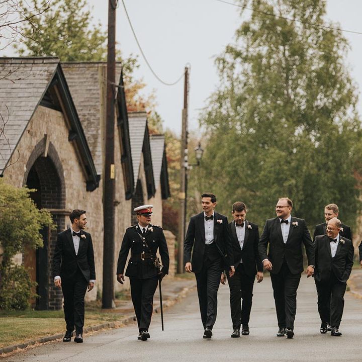 Groom walking with the groomsmen in matching black tie or military uniforms on the way to the church for the ceremony