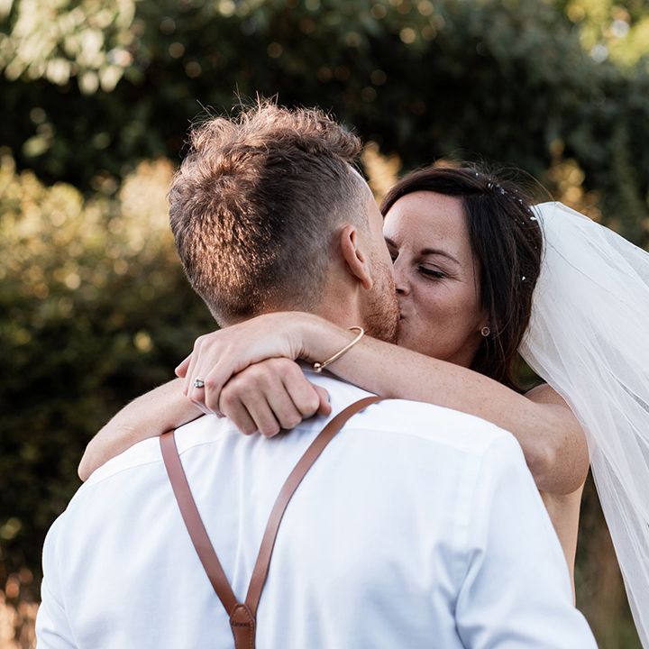 Bride in floor length veil kisses her groom outdoors during couples portraits after rustic barn wedding 