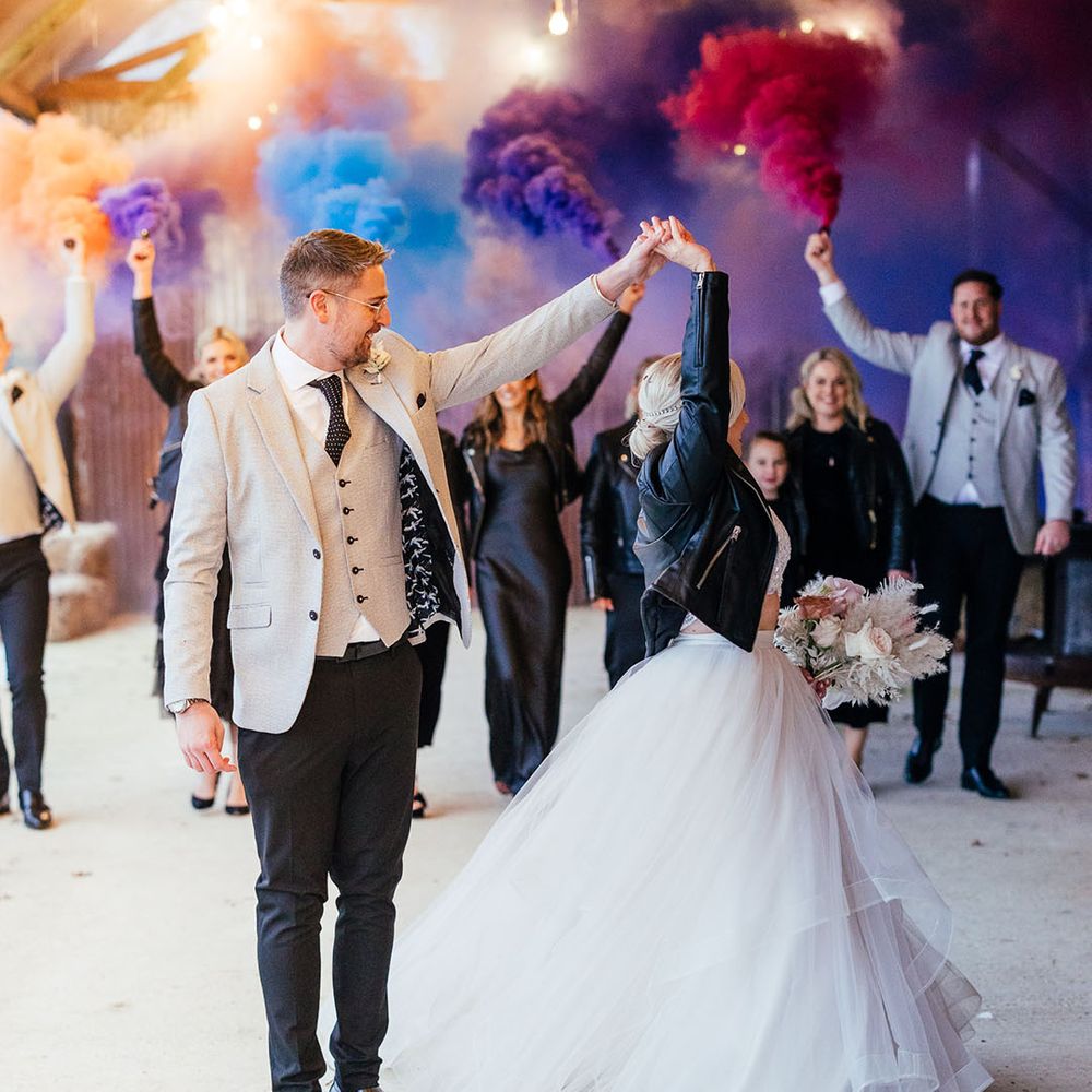 The groom spins the bride around wearing a leather jacket with colourful smoke bombs and the bridesmaids and groomsmen wearing matching black and grey outfits