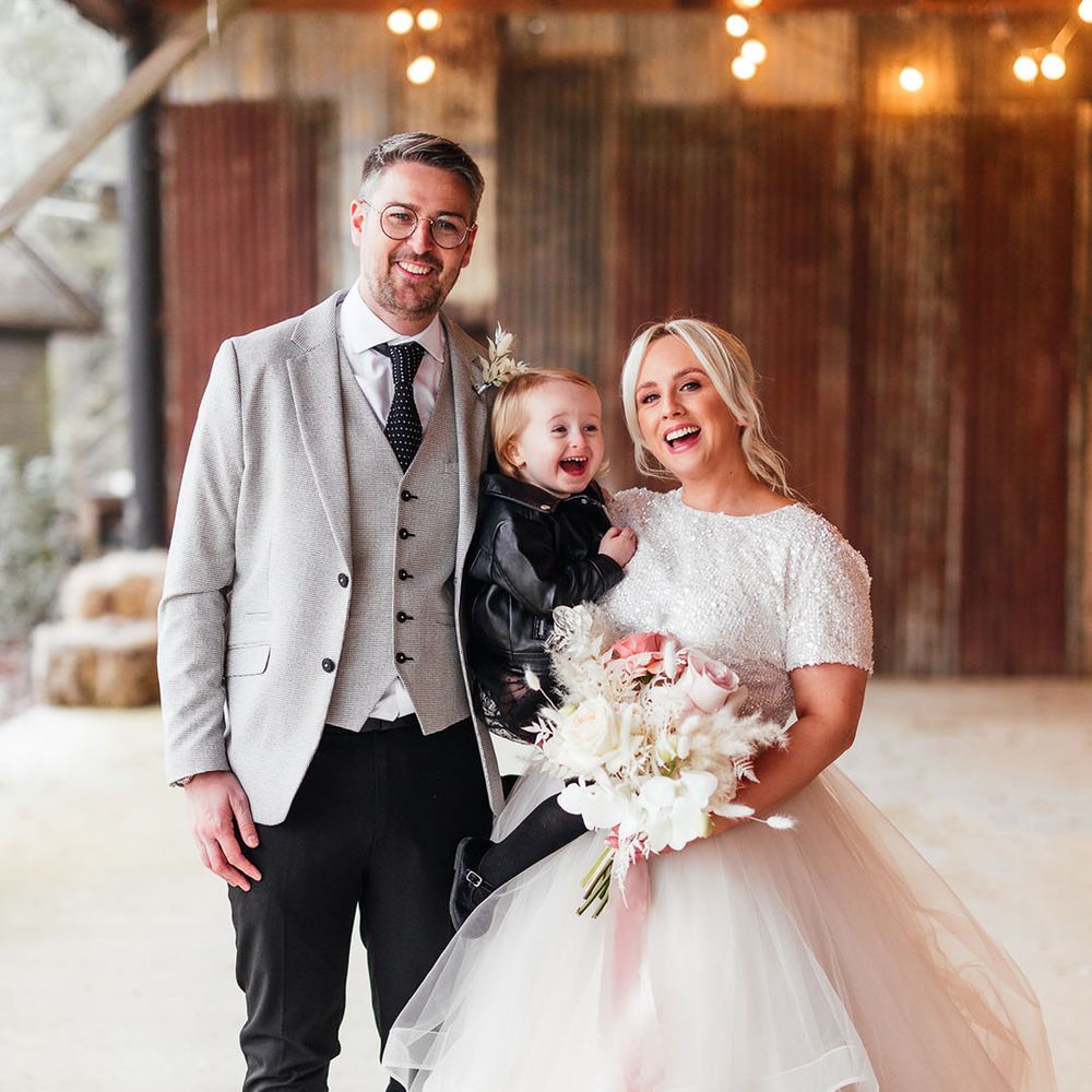 The bride and groom smile with their little girl wearing a black dress and black leather jacket to match the bridal party