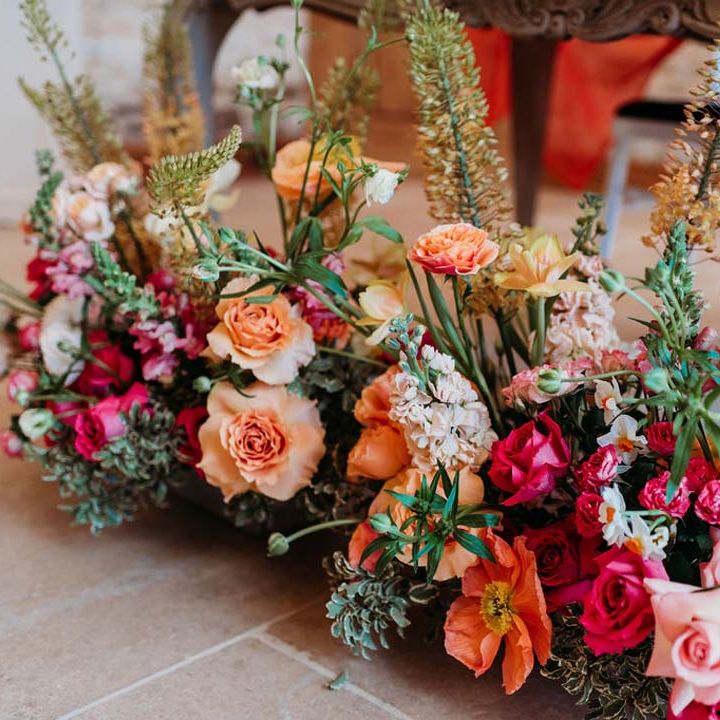 Seasonal wedding flower arrangement with pink and orange garden roses, orange floribunda, yellow ranunculus flowers, foliage and Iceland poppies 