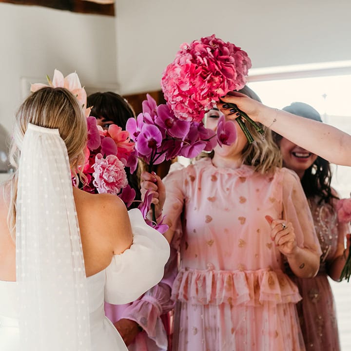 Bride wearing off the shoulder Jesus Peiro wedding dress with off the shoulder puff sleeves with the bridesmaids holding bright pink bouquets 
