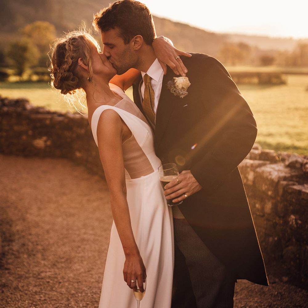 Golden hour sunset wedding photographs with groom in classic morning suit kissing bride in Andrea Hawke gown with mesh insert 