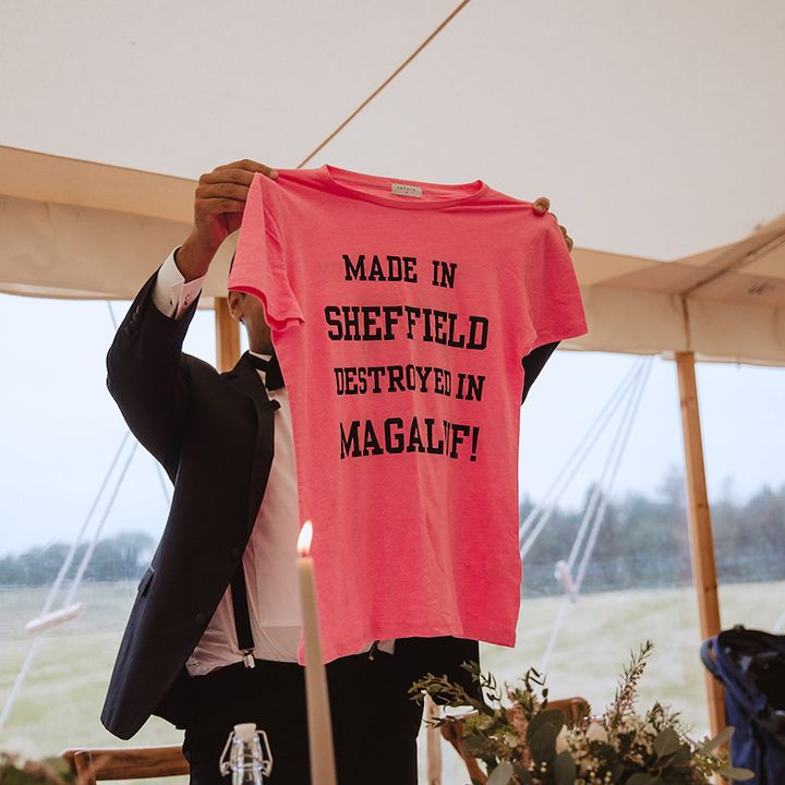 Groom holding up neon pink t shirt with black slogan 