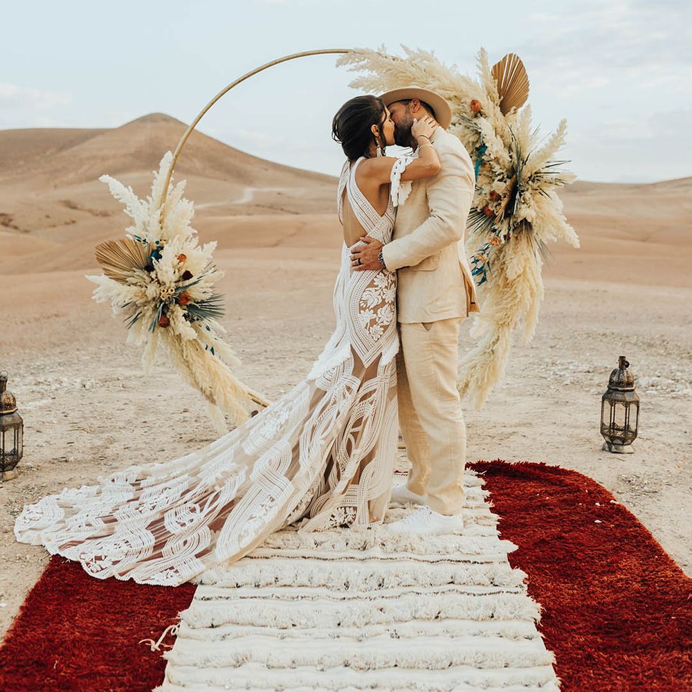 Bride in boho lace wedding dress kisses the groom in front of the boho moongate decoration 
