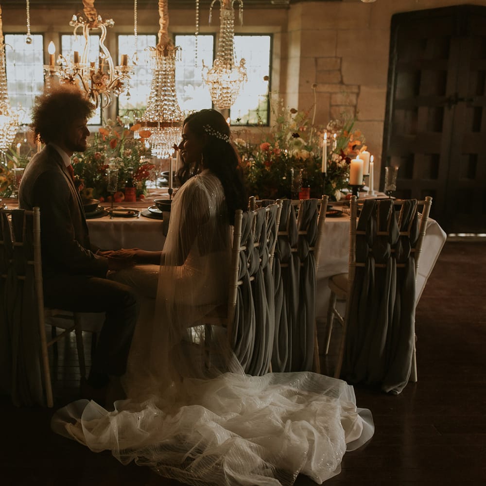 Bride and groom sitting at the intimate wedding reception filled with flowers and light