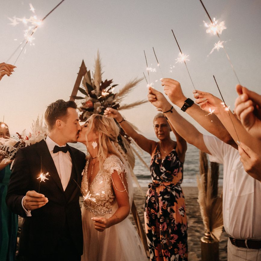 Bride and groom kiss under sparklers at beach wedding