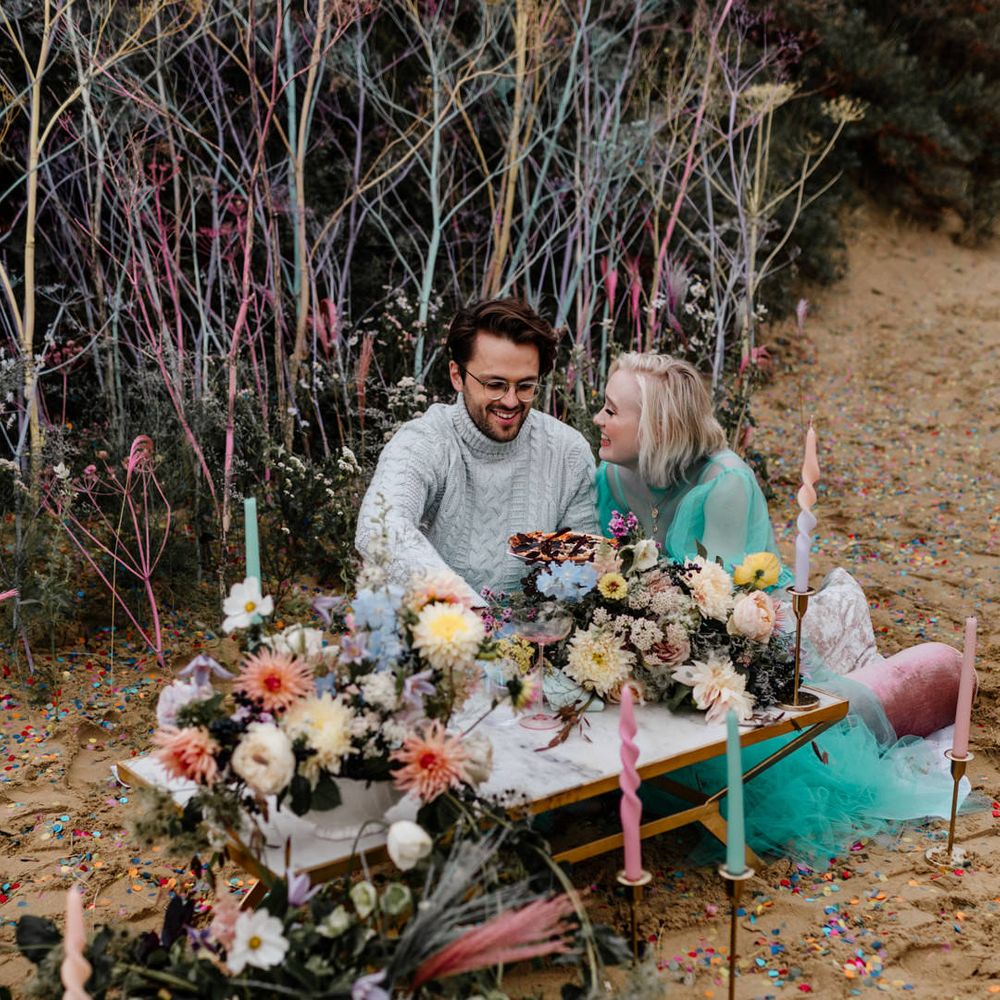 Bride and groom eating pizza on the beach at their intimate elopement with colourful flowers, candles and decor
