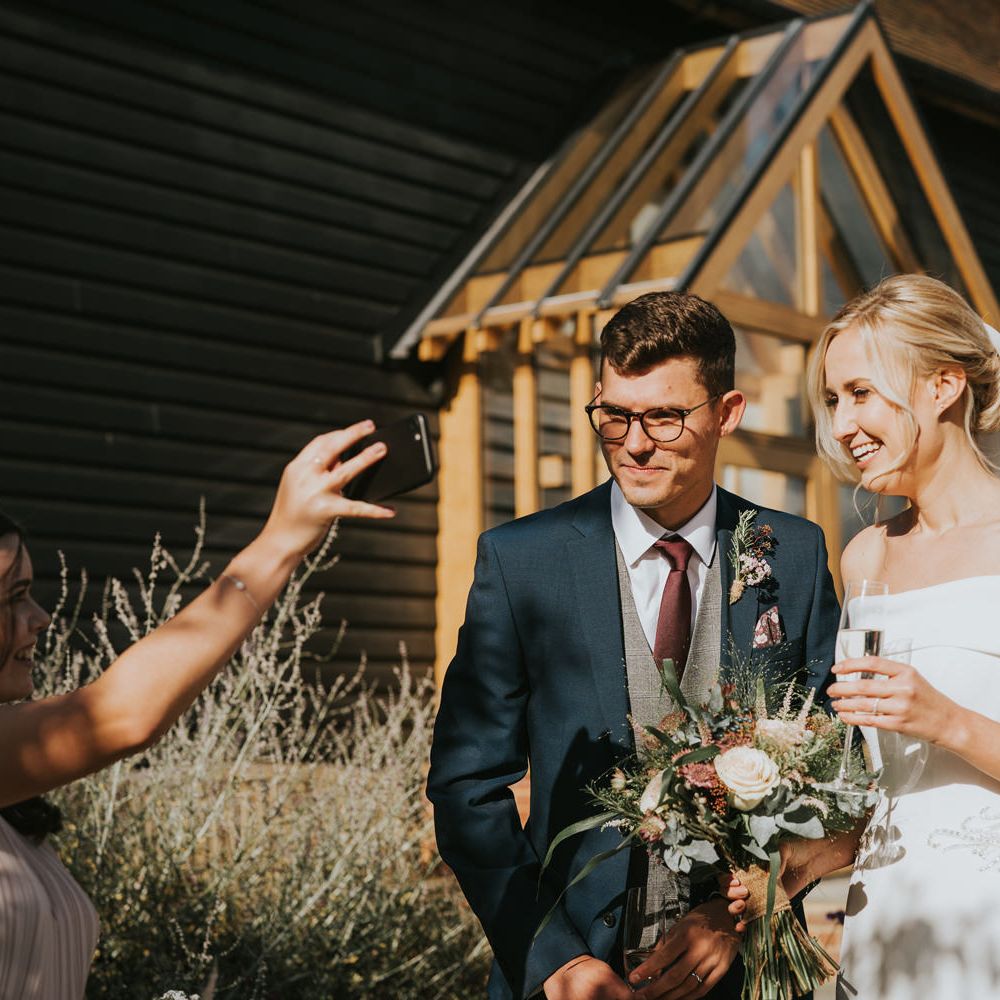 Bride & groom laugh with wedding guests in the sunshine