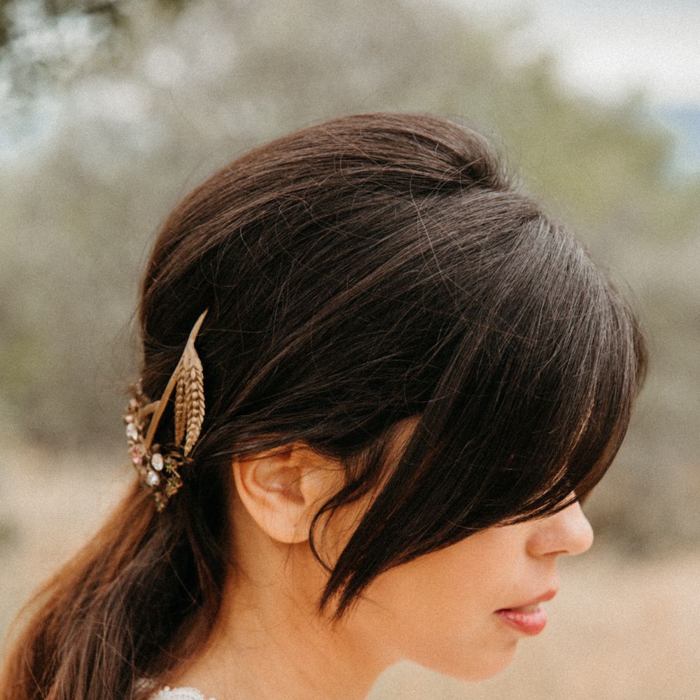 Dark haired bride wears her hair pulled back into a low ponytail complete with golden hair accessories 