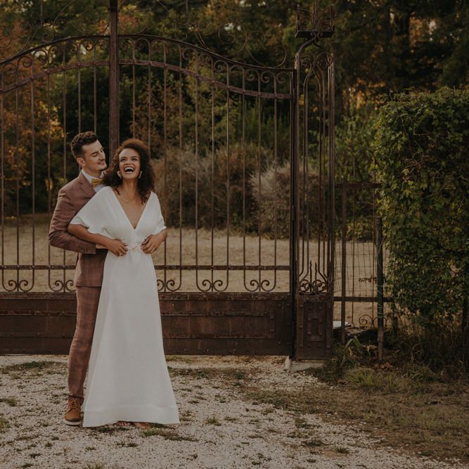 Groom in a brown wedding suit standing behind his bride at the gates of Château de Caumont