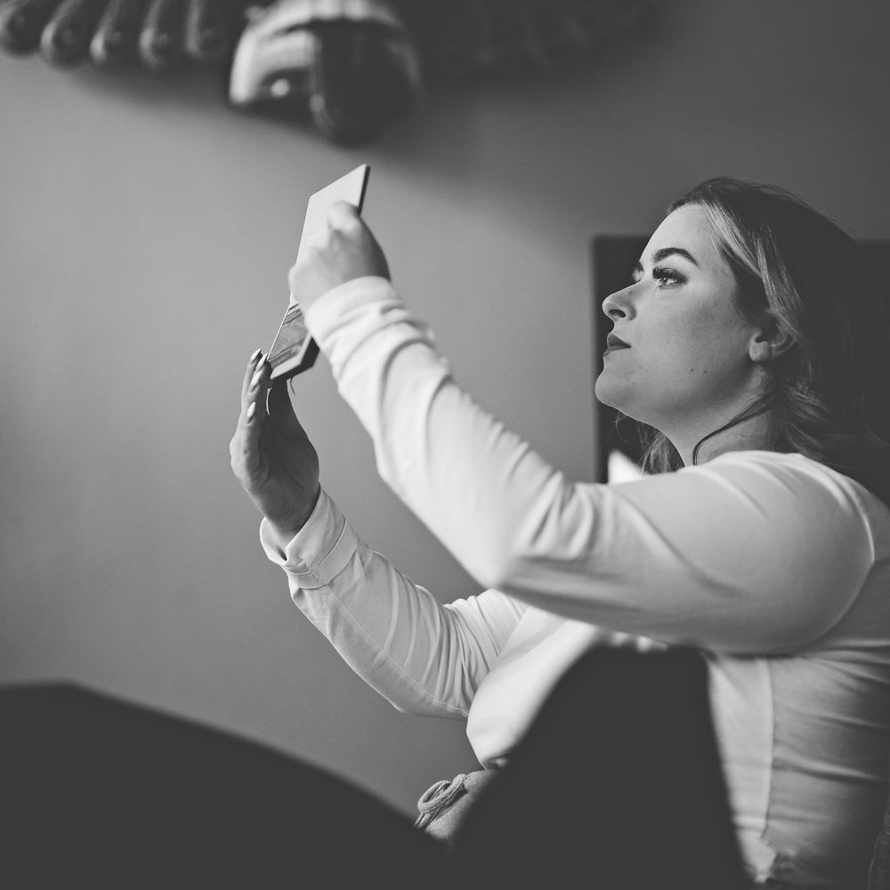 Black & white image of bride looking in mirror after applying makeup