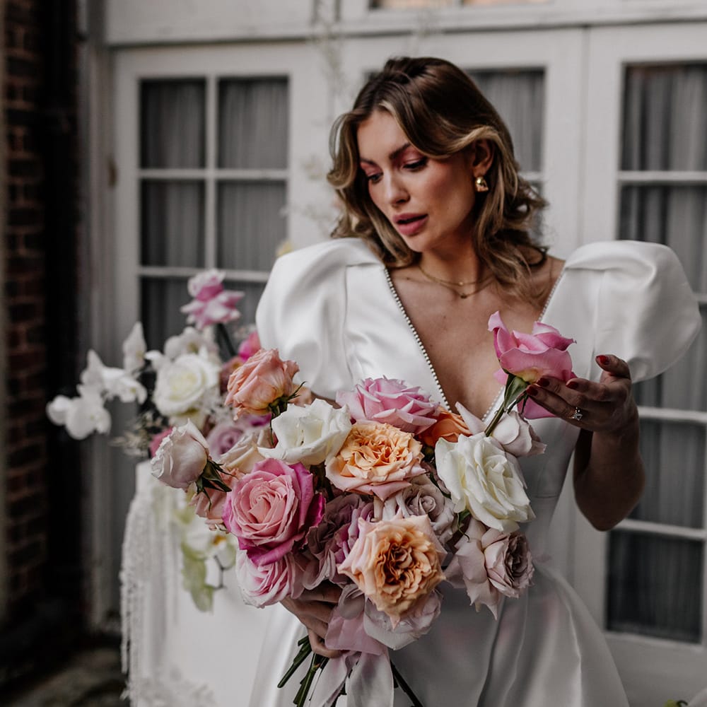 Bride in a Love In Lace bridal gown with plunging neckline holding her blush pink and white peel back rose wedding bouquet 