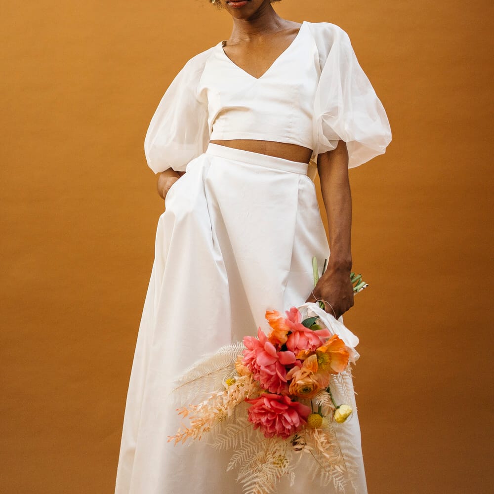 Bride wearing puff sleeve bridal separates holding a bouquet of pink flowers