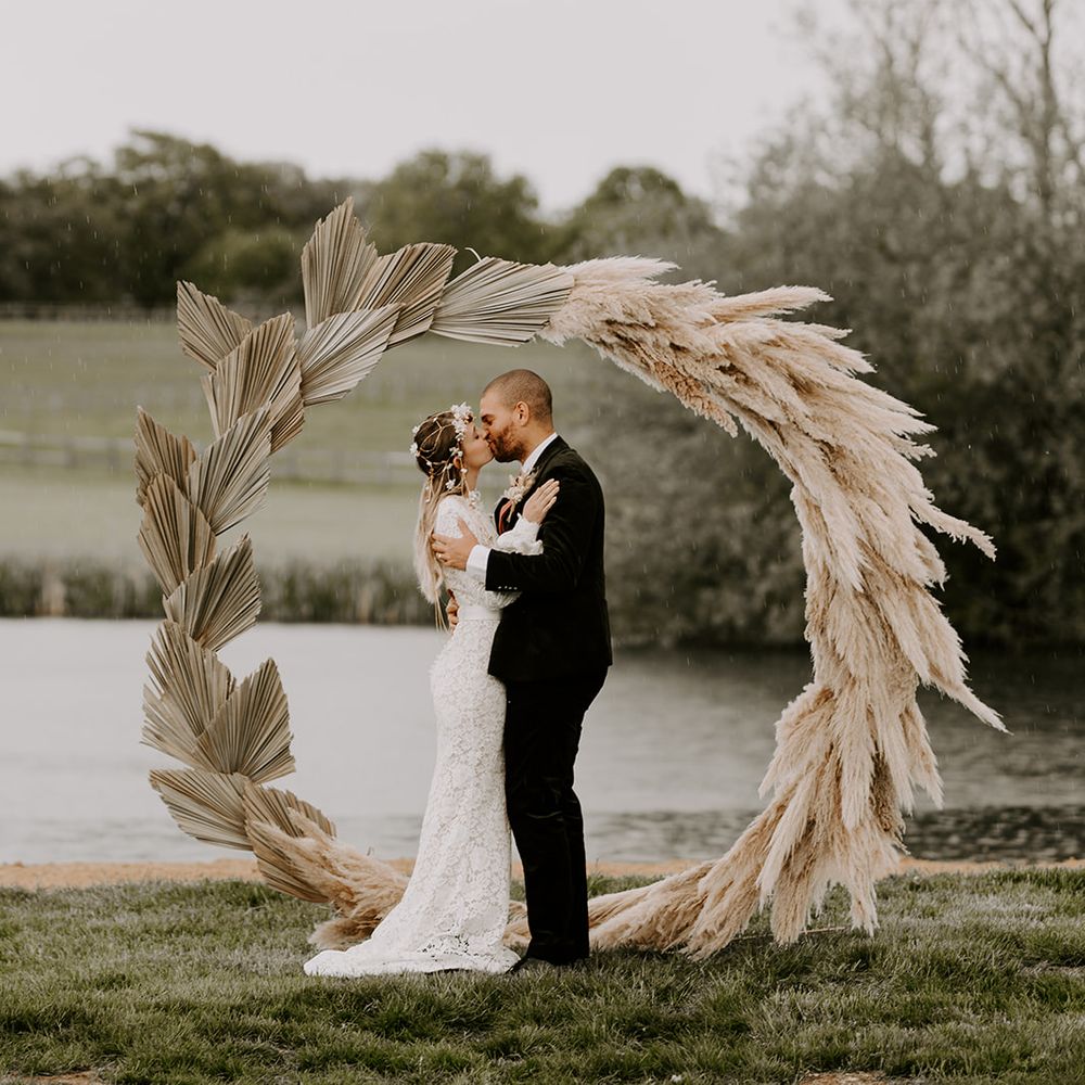 Bride and groom kissing in front of a dried palm leaf and pampas grass moon gate 