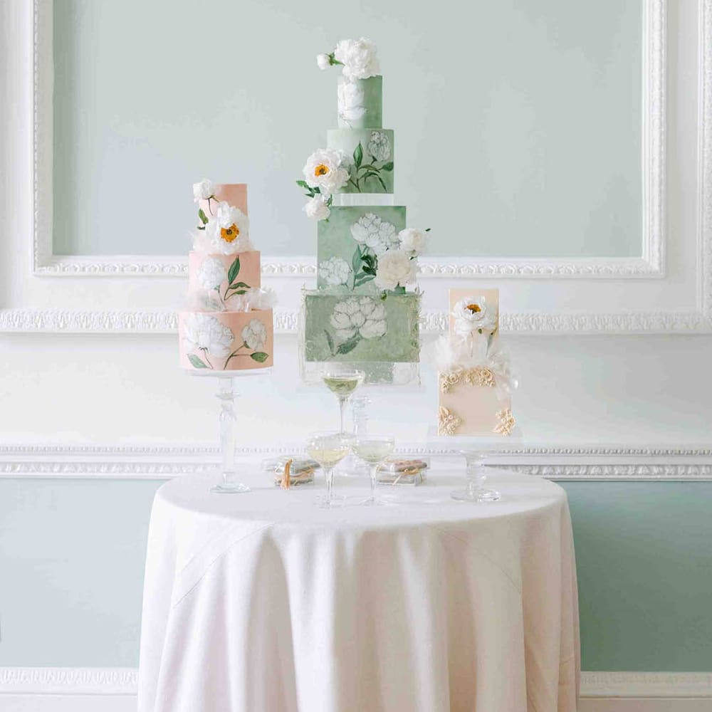 Wedding cake table with flower illustrated pastel pink and pale green wedding cakes with square and round tiers 